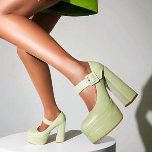 May include: Light green platform heels with a Mary Jane strap and buckle. The chunky heels and platform soles are a matching light green color. The shoes are made of a glossy material.