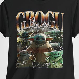 Può includere: T-shirt nera con una grafica di Grogu, noto anche come Baby Yoda, da The Mandalorian. Il design include più immagini di Grogu e il testo "GROGU Baby Yoda" in stile retrò.