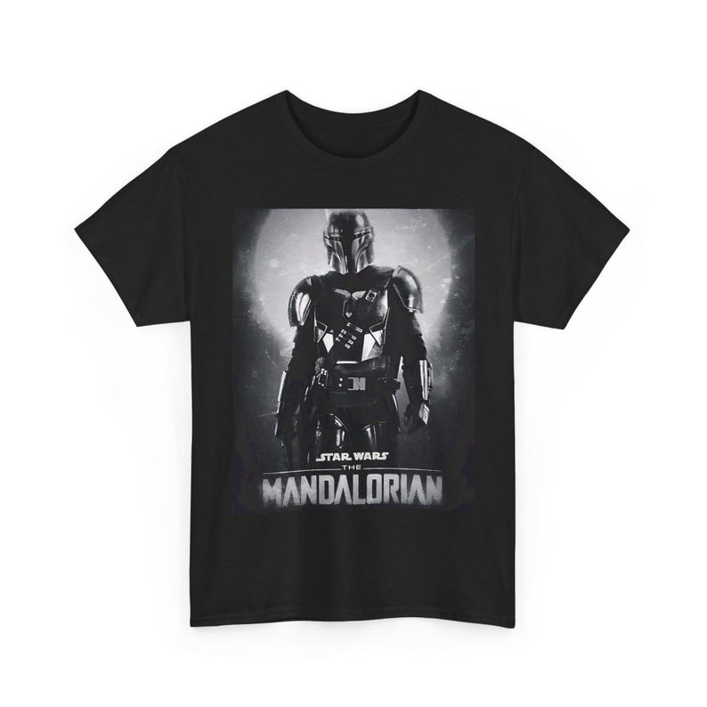 Può includere: T-shirt nera con un'immagine in scala di grigi di The Mandalorian di Star Wars. L'immagine mostra il personaggio con l'armatura completa su uno sfondo illuminato dalla luna. Le parole "STAR WARS" e "THE MANDALORIAN" sono stampate sotto.