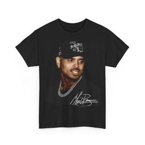 Può includere: Una t-shirt nera a maniche corte con una stampa fotografica di Chris Brown che indossa un berretto da baseball nero e una catena d'argento. La grafica include una firma bianca in corsivo in basso a destra sul tessuto nero.