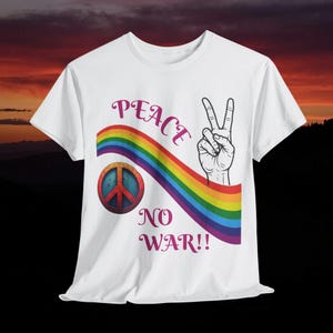 May include: White t-shirt with a peace sign design. The design includes a rainbow, a peace symbol, and a hand making the peace sign gesture. The words "PEACE NO WAR!!" are written in a purple script font.