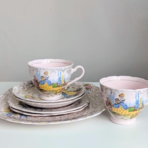 Może przedstawiać: Zestaw do herbaty w stylu vintage z dwiema różowymi filiżankami i spodkami z kwiatowym i figuralnym wzorem. Zestaw zawiera tacę do serwowania i dodatkowe spodki, idealne na przyjęcie herbaciane lub wystawę.