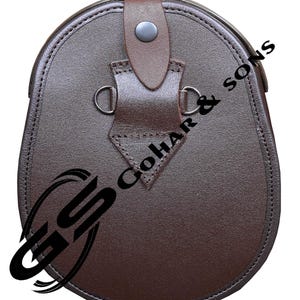 Pu&ograve; includere: Un sporran in pelle marrone con fondo arrotondato e chiusura a patta. Presenta un cinturino decorativo con un bottone e due anelli metallici. Il testo "GoHar & Sons" &egrave; visibile in basso a sinistra.
