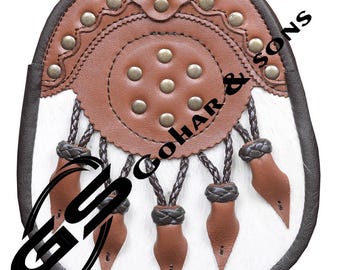 Può includere: Un sporran in pelle marrone e bianca con borchie decorative in metallo e nappe intrecciate. Lo sporran ha un design circolare al centro ed è visibile il testo "GOHAR & SONS".