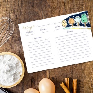 May include: A white recipe card with gold script and a watercolor illustration of trees. The card has sections for prep time, cook time, ingredients, servings, and directions. The card is on a wooden surface with baking ingredients.