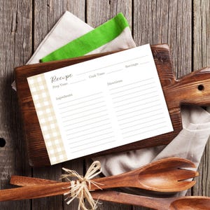 Puede incluir: Una tarjeta de recetas con la palabra "Receta" en la parte superior, con espacios para el tiempo de preparación, los ingredientes, el tiempo de cocción, las porciones y las instrucciones. La tarjeta tiene un patrón de cuadros beige en el lado izquierdo. Descansa sobre una tabla de cortar de madera con cucharas de madera y una servilleta de lino.