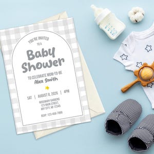 May include: A baby shower invitation with a gray gingham pattern, featuring the text "Baby Shower" and event details. Accompanying items include a baby bottle, a white onesie with star designs, a wooden rattle, and striped baby slippers, all on a light blue surface.