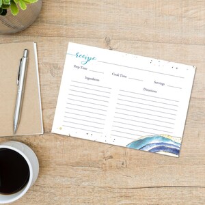 May include: A white recipe card with a watercolor design in shades of blue and gold. The word "recipe" is written in teal script. The card has sections for prep time, cook time, ingredients, servings, and directions. A pen, notebook, and coffee cup are also visible.