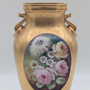 May include: A gold vase with a painted floral design. The oval painting features pink and white roses and other flowers. The vase has two handles and a textured surface. The vase is decorated with a gold pattern.