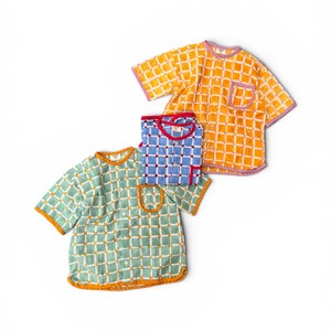 May include: Three short-sleeved button-down shirts featuring a grid pattern. One shirt is orange with white lines and purple trim, one is blue with white lines and red trim, and one is light green with white lines and orange trim, each with a pocket.