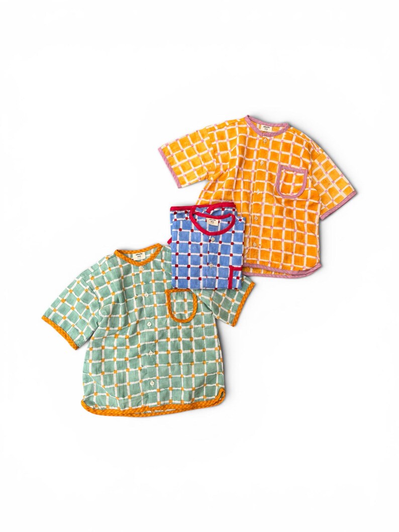 May include: Three short-sleeved button-down shirts featuring a grid pattern. One shirt is orange with white lines and purple trim, one is blue with white lines and red trim, and one is light green with white lines and orange trim, each with a pocket.