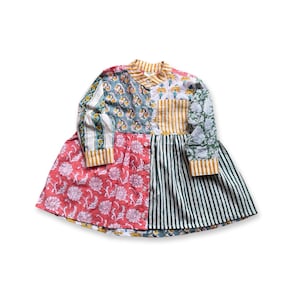 Puede incluir: Vestido patchwork con una variedad de estampados florales y a rayas en tonos rojos, verdes, azules y amarillos. El vestido tiene mangas largas con puños a rayas y cuello. La falda es una mezcla de paneles florales y a rayas.