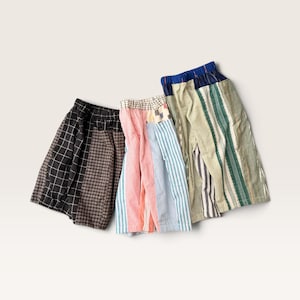 Puede incluir: Tres pares de pantalones cortos con diseños de patchwork. El primer par tiene patrones de cuadrícula y cuadros en blanco y negro. El segundo par presenta rayas verticales en rojo, blanco y azul. El tercero muestra rayas verdes, blancas y azules.