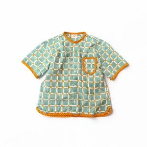 May include: A short-sleeved button-down shirt featuring a light green and white grid pattern with small orange squares at the intersections. The shirt has an orange trim along the collar, sleeve cuffs, hem, and the single chest pocket.