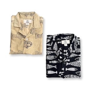 Puede incluir: Dos camisas abotonadas con estampados de peces. Una camisa es beige con peces negros, la otra es negra con peces blancos. Ambas camisas tienen cuello y una etiqueta que dice "3-4".