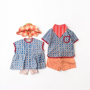 May include: A set of children's clothing including a blue and white checkered sleeveless top with red trim, a matching blue and white checkered short-sleeve button-down shirt with a red pocket, solid peach shorts, a red striped bandana, and a hat.