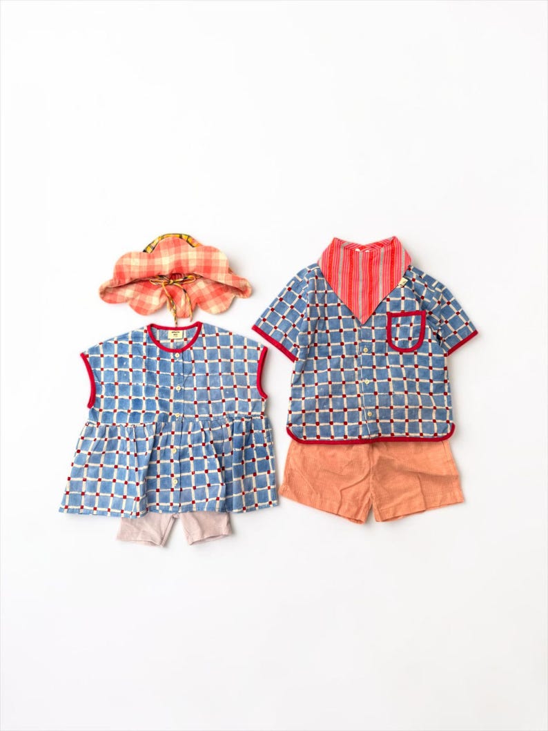 May include: A set of children's clothing including a blue and white checkered sleeveless top with red trim, a matching blue and white checkered short-sleeve button-down shirt with a red pocket, solid peach shorts, a red striped bandana, and a hat.