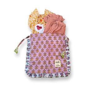 Può includere: Un sacco con coulisse lavanda con un motivo floreale dorato, contenente abbigliamento. All'interno della borsa ci sono un top floreale giallo e pantaloncini color pesca. La borsa ha un bordo fantasia e un'etichetta con la scritta "saruche".