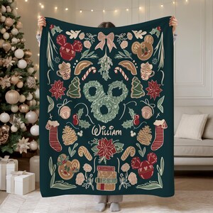 Puede incluir: Una manta de color verde oscuro con un dise&ntilde;o navide&ntilde;o festivo, que incluye hombres de jengibre con el tema de Mickey Mouse, adornos y flores de pascua. El nombre "William" se muestra en una fuente cursiva. La manta est&aacute; decorada con elementos navide&ntilde;os.