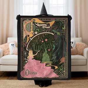 May include: Black blanket featuring a colorful illustration with the word "Wicked". The design includes a princess in a pink gown, a green witch, and a green castle. The blanket has a decorative border and the name "Olivia" is written on the blanket.