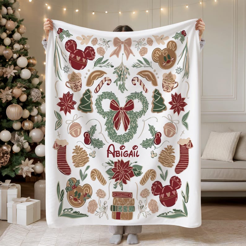 Puede incluir: Manta blanca con un dise&ntilde;o festivo con formas de Mickey Mouse, hombres de jengibre, &aacute;rboles de Navidad y bastones de caramelo. El nombre "Abigail" est&aacute; escrito en cursiva. La manta tiene un tema navide&ntilde;o con acentos rojos, verdes y marrones.