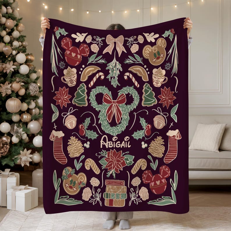 Puede incluir: Una manta de color p&uacute;rpura oscuro con un dise&ntilde;o navide&ntilde;o festivo. La manta est&aacute; adornada con ilustraciones tem&aacute;ticas de vacaciones, que incluyen figuras de pan de jengibre, bastones de caramelo, flores de Nochebuena y una corona. El nombre "Abigail" est&aacute; escrito en cursiva.