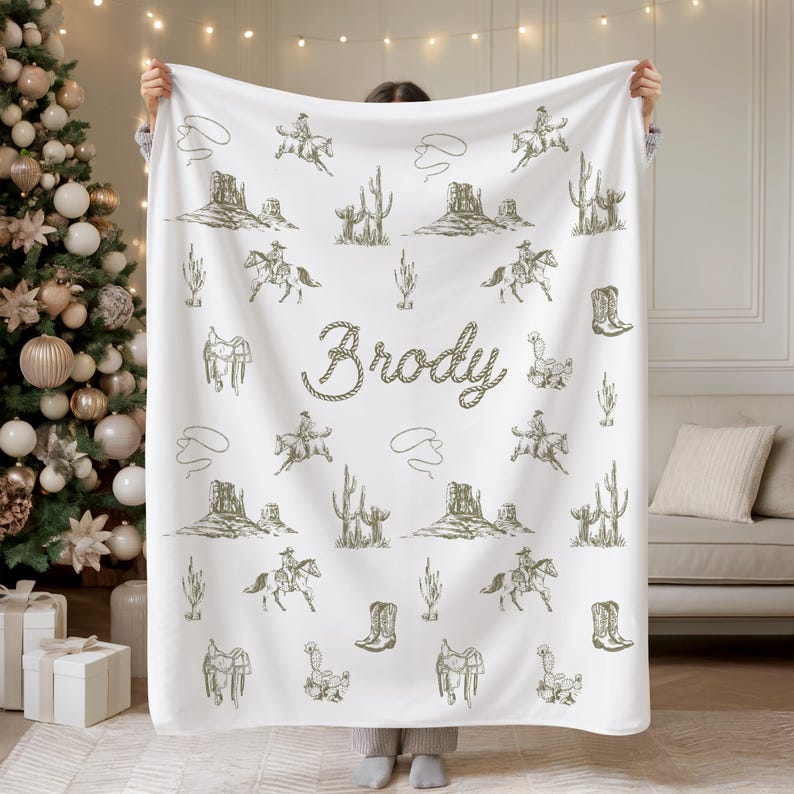 Peut inclure: Couverture blanche orn&eacute;e d'un motif r&eacute;p&eacute;t&eacute; de cowboys &agrave; cheval, de cactus et de paysages d&eacute;sertiques verts. Le nom "Brody" est &eacute;crit en police de style corde. Une couverture sur le th&egrave;me du western.