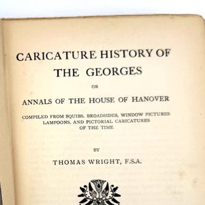Puede incluir: Libro abierto, "CARICATURE HISTORY OF THE GEORGES", con ilustraciones. La página izquierda muestra un dibujo en blanco y negro de un hombre observando una figura en miniatura. Nueva edición publicada en Londres en 1904.