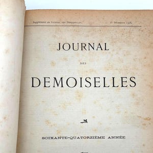 Może przedstawiać: Otwarta, zabytkowa książka z tytułem "JOURNAL DES DEMOISELLES" dużymi czarnymi literami. Okładka ma beżowy odcień z plamami starości. Widoczny jest również tekst "SOIXANTE-QUATORZIÈME ANNÉE". Książka pochodzi z Paryża, 1906.