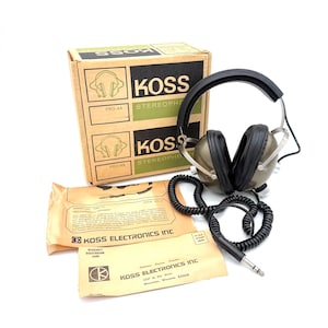 May include: Vintage Koss Pro-4A stereo headphones with original packaging. The headphones have black earcups and a silver headband. The box and paperwork are tan and green, with the Koss logo and product information.