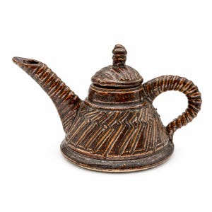 May include: A dark brown ceramic teapot with a glossy finish, featuring a wide base, a long angled spout, and a curved handle. The body, spout, and handle are decorated with deep, carved geometric zigzag patterns and a matching lidded top.