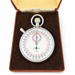 May include: A silver Zodex 1/10 7 jewels stopwatch with a white face, black and red numerals, and a winding crown, presented in a brown velvet-lined case. The dial features a secondary sub-dial and a side-mounted pusher for time measurement.
