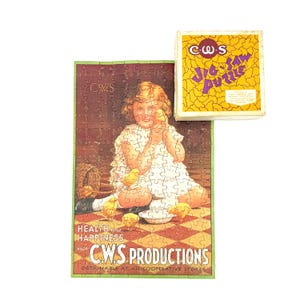 Puede incluir: Un rompecabezas vintage C.W.S. que muestra a un niño con vestido blanco rodeado de pollitos amarillos sobre un suelo de cuadros rojos y blancos. La caja es amarilla con un patrón agrietado y texto morado que dice C.W.S. JIG-SAW PUZZLE. El texto del rompecabezas dice HEALTH AND HAPPINESS with C.W.S. PRODUCTIONS.