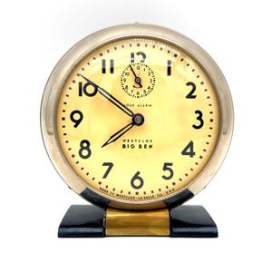 Op de afbeelding: Vintage Westclox Big Ben wekker met een crèmekleurige wijzerplaat en zwarte cijfers. De klok heeft een zilverkleurige metalen behuizing en een zwarte basis met gouden accenten. De wijzerplaat leest "LOUD ALARM" en "MADE BY WESTCLOX LA SALLE ILL U.S.A."