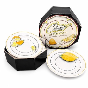 May include: A set of white ceramic plates with a lemon design, presented in a black octagonal box. The plates feature a black and gold rim and a lemon illustration. The box has text that reads "Citron de France".