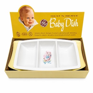 Puede incluir: Un juego de platos para bebés vintage en su caja original. El plato blanco dividido presenta un gráfico de conejito y está etiquetado como "HEAT 'N SERVE Baby Dish". La caja es amarilla con una imagen de bebé y texto. El plato está diseñado para mantener la comida caliente y es fácil de limpiar.