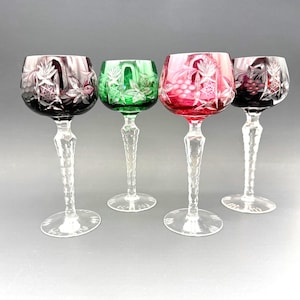 May include: Four coloured wine glasses with clear, textured stems and bases. The bowls are in shades of red, green, and purple, with etched floral and geometric designs. The glasses are for serving wine.