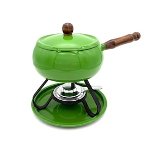 Op de afbeelding: Een groene fonduepan met een houten handvat en dekselknop. De pan staat op een zwart metalen standaard met een bijpassende groene basis. Een kleine, zilveren brander is zichtbaar eronder.