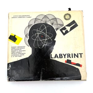 May include: Vintage book cover featuring a black silhouette of a person with an atom design inside the head. The title "LABYRINT" is in white, with author names listed below. The cover has a retro, mid-century modern design with geometric shapes.