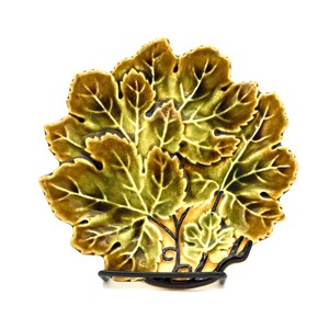 May include: A decorative leaf-shaped plate with a detailed design. The plate features a layered arrangement of green and brown leaves with intricate vein patterns. It is supported by a black metal stand, creating a unique display piece.