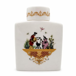 May include: A white ceramic jar with a matching lid, featuring a gold decorative border on the lid and a central illustration of two figures in traditional attire interacting near a small tripod vessel, accented by a gold ornamental base design.