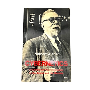 Puede incluir: Portada de libro vintage con un retrato en blanco y negro de Norbert Wiener. El título "CYBERNETICS" está en rojo. El libro trata sobre el control y la comunicación en animales y máquinas.