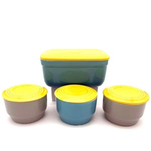 Może przedstawiać: Zestaw czterech ceramicznych pojemników do przechowywania żywności. Pojemniki są w odcieniach niebieskiego, szarego i zielonego, z jaskrawożółtymi pokrywkami. Pojemniki mają różne rozmiary i kształty.