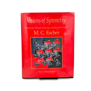 Może przedstawiać: Czerwona książka zatytułowana "Visions of Symmetry" autorstwa M.C. Eschera. Okładka przedstawia kolorowy wzór ryb w kwadratowej ramie. Książka jest w twardej oprawie i jest prezentowana na białym tle.