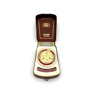 May include: Vintage Zeiss Ikon Ikophot light meter in a brown leather case. The meter has a white and red dial with various scales and the text "IKOPHOT". The case is open, revealing the meter and the text "ZEISS IKON STUTTGART Germany".