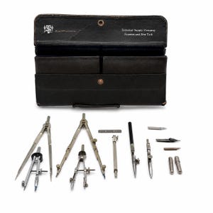 May include: A vintage black leather drafting instrument case with the text Technical Supply Company Scranton and New York, accompanied by a collection of metal compasses, dividers, ruling pens, and interchangeable nibs arranged on a surface.