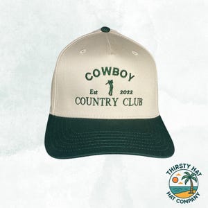 Puede incluir: Una gorra de b&eacute;isbol beige y verde con el texto "COWBOY COUNTRY CLUB" bordado en la parte delantera. El texto "Est 2022" tambi&eacute;n est&aacute; bordado en la parte delantera. Una silueta de golfista est&aacute; bordada entre el texto.