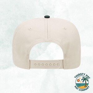 Puede incluir: Una gorra de b&eacute;isbol beige con la parte superior negra y una correa ajustable negra con la palabra "DEVO" impresa.