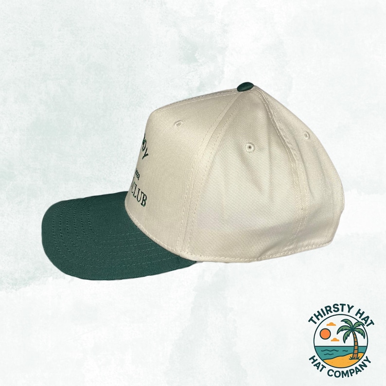 Puede incluir: Una gorra de b&eacute;isbol blanca y verde con el texto "The Country Club" bordado en la parte delantera. La gorra tiene una visera verde y una corona blanca.
