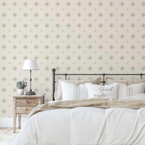 May include: A bedroom scene featuring a bed with white bedding, pillows, and a beige throw. The headboard is black metal. The wall has a cream-colored wallpaper with a repeating pattern of green starbursts and small circles. A nightstand with a lamp and a small plant is on the left.
